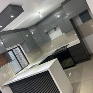 Modern custom-designed luxury kitchen in Dubai featuring matte dark grey cabinetry, warm wooden breakfast bar, pendant lighting, integrated shelving, and minimalist contemporary interior design. Modern custom-designed luxury kitchen in Dubai featuring matte dark grey cabinetry, warm wooden breakfast bar, pendant lighting, integrated shelving, and minimalist contemporary interior design.